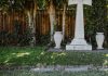 A serene cemetery scene with a prominent cross tombstone under lush trees.