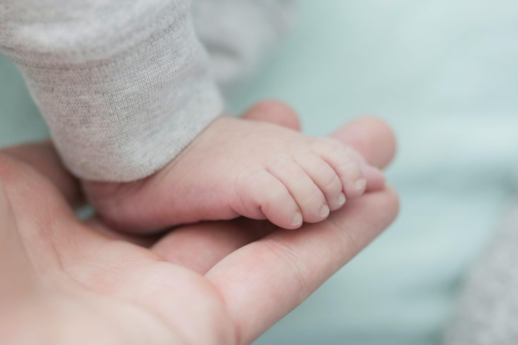 Baby wearing gray bottoms on person hand